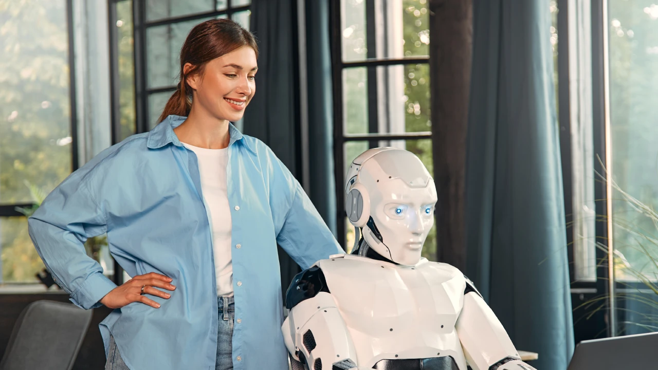 Young woman with a cup of coffee and a humanoid robot working while sitting at a laptop in a modern office. Collaboration between humans and artificial intelligence.